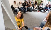 Une femme avec un t-shirt jaune de FRAGILE écrit sur un flipchart, des personnes la regardent