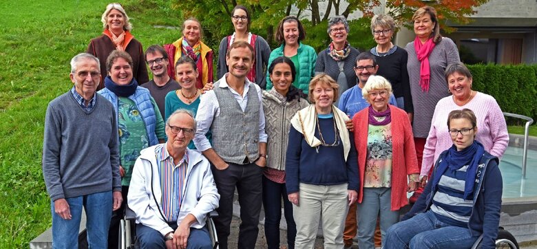 Eine Gruppe von Menschen stellt sich für ein Gruppenbild auf. Zwei Personen im Vordergrund sitzen im Rollstuhl.