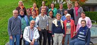 Eine Gruppe von Menschen stellt sich für ein Gruppenbild auf. Zwei Personen im Vordergrund sitzen im Rollstuhl.