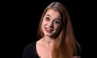 Eine Frau mit langen Haaren lächelt und blickt zur Seite vor dunklem Hintergrund.