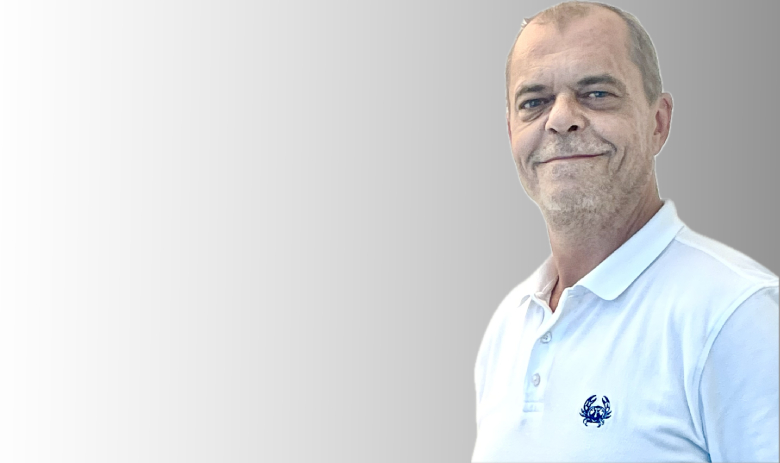 Mike B. Portrait eines Mannes. Er steht halb seitlich und blickt in die Kamera. Der Hintergrund ist ein Weiss-Grauer Verlauf.