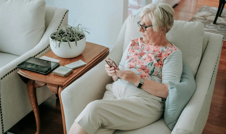 Femme tenant un téléphone Une femme est assise dans son salon sur un fauteuil, les yeux rivés sur son téléphone portable.