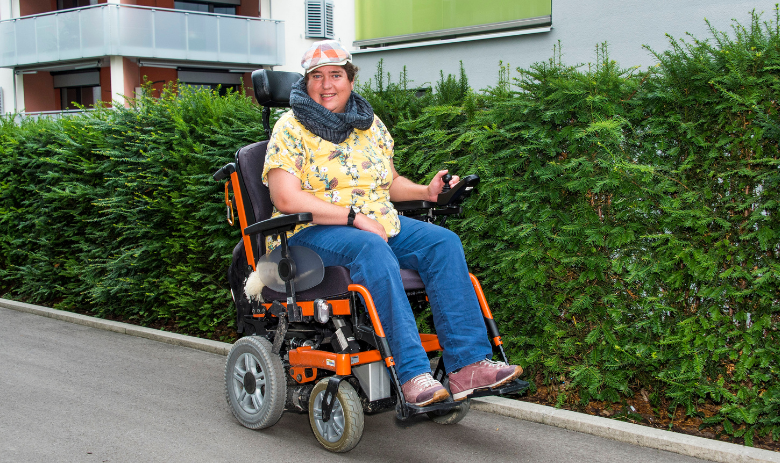 Inklusion Eine Frau fährt mit dem Elektro-Rollstuhl auf der Strasse.
