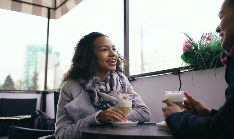 Recherche de partenaire Une femme avec des cheveux bouclés tient une boisson dans sa main, elle discute avec une autre personne